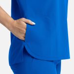 A bright blue women's top with three pockets, featuring a side slit and a relaxed fit. It has a logo on it.