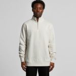 A man is wearing a cream-coloured half zip crew jumper with a relaxed fit, featuring a stand-up collar.