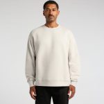 A light grey sweater on a man, featuring a relaxed fit and long sleeves. The garment has a logo on it.