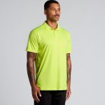 A man wearing a bright yellow polo shirt stands against a light background. The shirt has a logo on it.