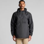 A man wearing a black windbreaker jacket featuring a hood and front pocket. The jacket has a logo on it.