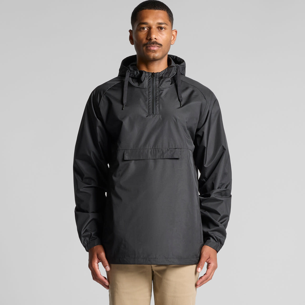 A man wearing a black windbreaker jacket featuring a hood and front pocket. The jacket has a logo on it. A man wearing a black windbreaker jacket featuring a hood and front pocket. The jacket has a logo on it.