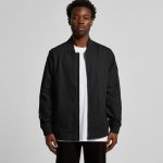 A black bomber jacket worn by a model, featuring a zip front and ribbed cuffs, with a logo visible.