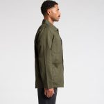 A man wearing an olive green canvas chore jacket, viewed from the side, with a simple design and a logo present.