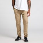 Beige pants are displayed on a model standing with hands in pockets, wearing a white t-shirt and black shoes.