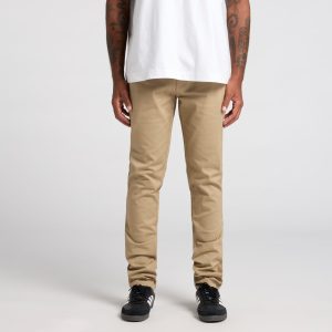 Beige standard pants worn by a person with tattoos, paired with black sneakers and a white t-shirt.