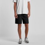 Black sports shorts with an elastic waistband, modelled by a person wearing a white t-shirt and grey sneakers.