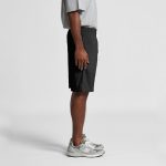 A pair of black sports shorts with a drawstring waist, shown on a model from the side. The model is wearing grey sneakers.
