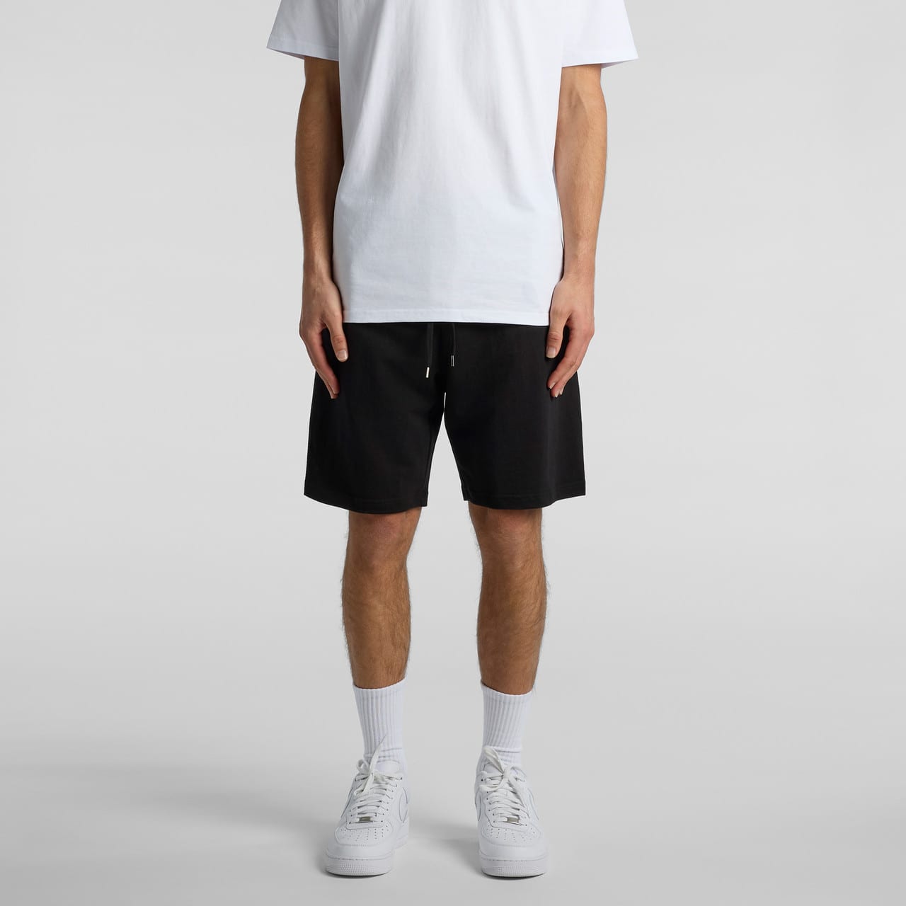 A person wearing black sports shorts styled with a plain white t-shirt and white sneakers. A person wearing black sports shorts styled with a plain white t-shirt and white sneakers.