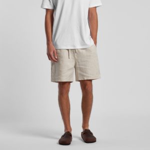 Linen shorts in a light beige colour, featuring an elastic waistband and a casual fit. A model stands wearing them with a white t-shirt.