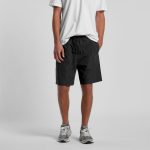 Black sports shorts with an elastic waistband, modelled by a person wearing a white t-shirt and grey sneakers.