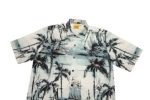 A short-sleeved shirt featuring a blue and white tropical print with palm trees and sailing ships. It has a collar and buttons.