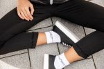 Organic sneaker socks in white, worn with black sneakers and black cropped pants on a grey tiled surface.