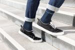 A pair of navy organic socks worn with black shoes, standing on outdoor steps with rolled-up denim jeans.