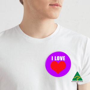 A purple button badge featuring a red heart design, attached to a white shirt on a plain background.