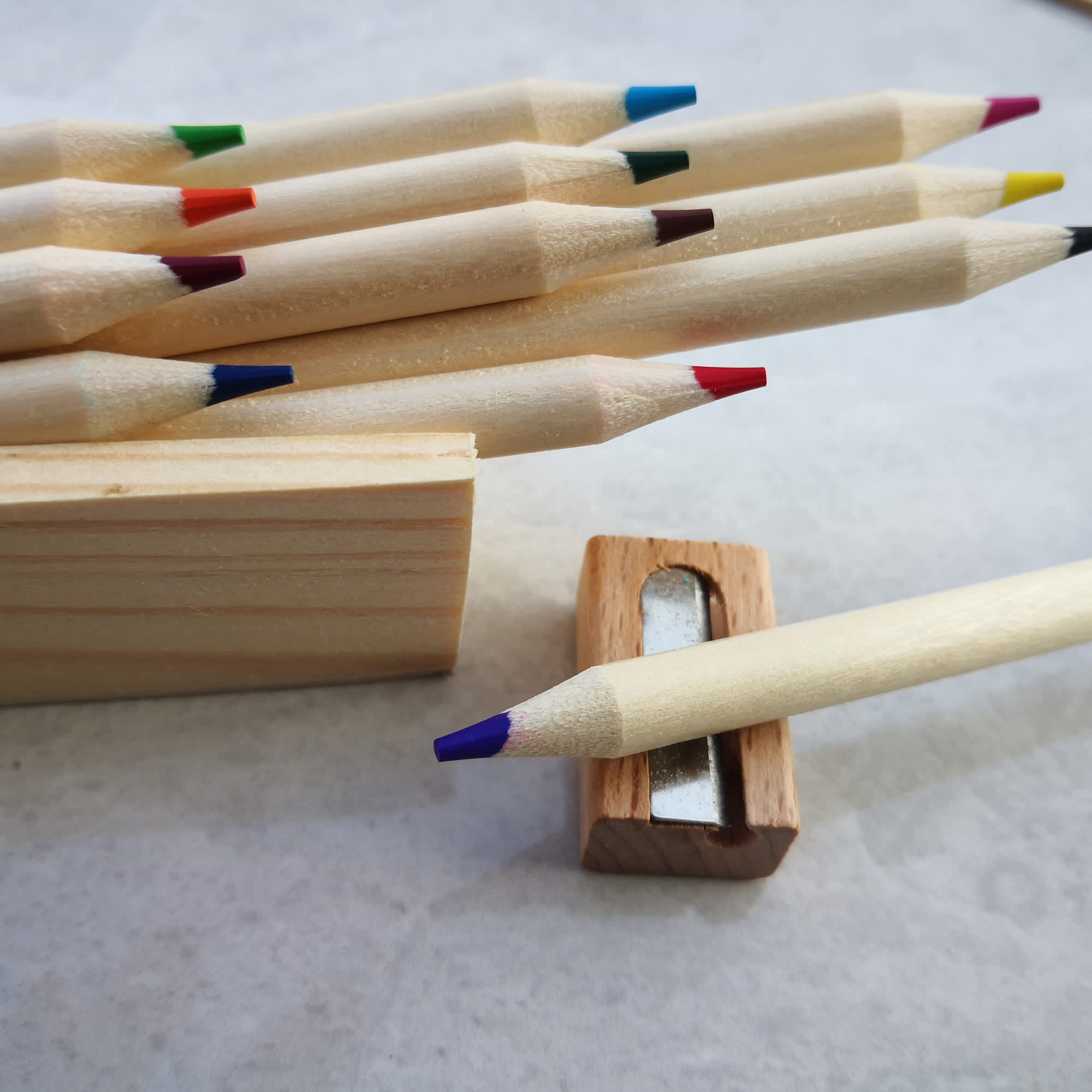 A set of wooden coloured pencils in various hues, with a sharpener alongside some of the pencils. Yat Colouring Pencil Set - Image 1