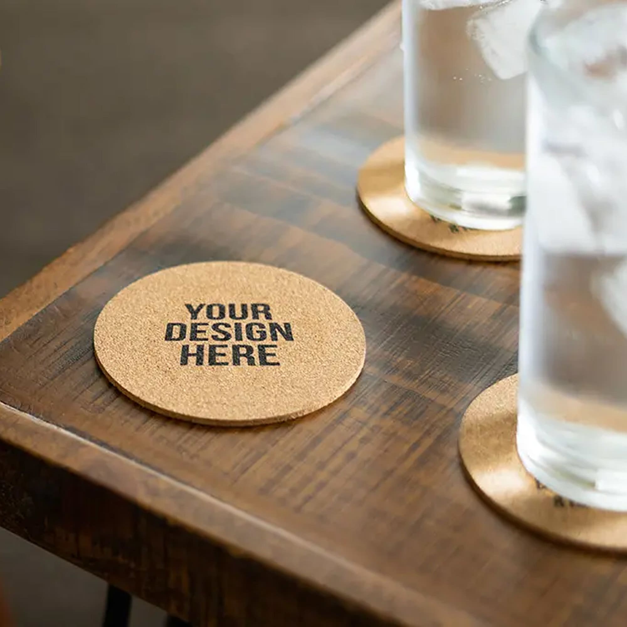 A round cork coaster on a wooden table with two glasses of water and a logo on the coaster. Vineyards Cork Coaster-Round - Image 1
