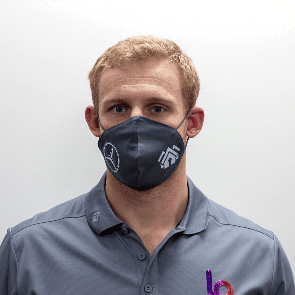 A grey face mask featuring a logo, worn by a person with short light hair and a grey shirt. Viroblock Face Mask - Image 1