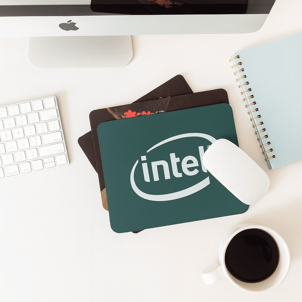 A green fabric mouse mat with a logo, placed on a desk alongside a white mouse, coffee cup, and notebook. Fabric Mouse Mat (225mm x 185mm) - Image 1