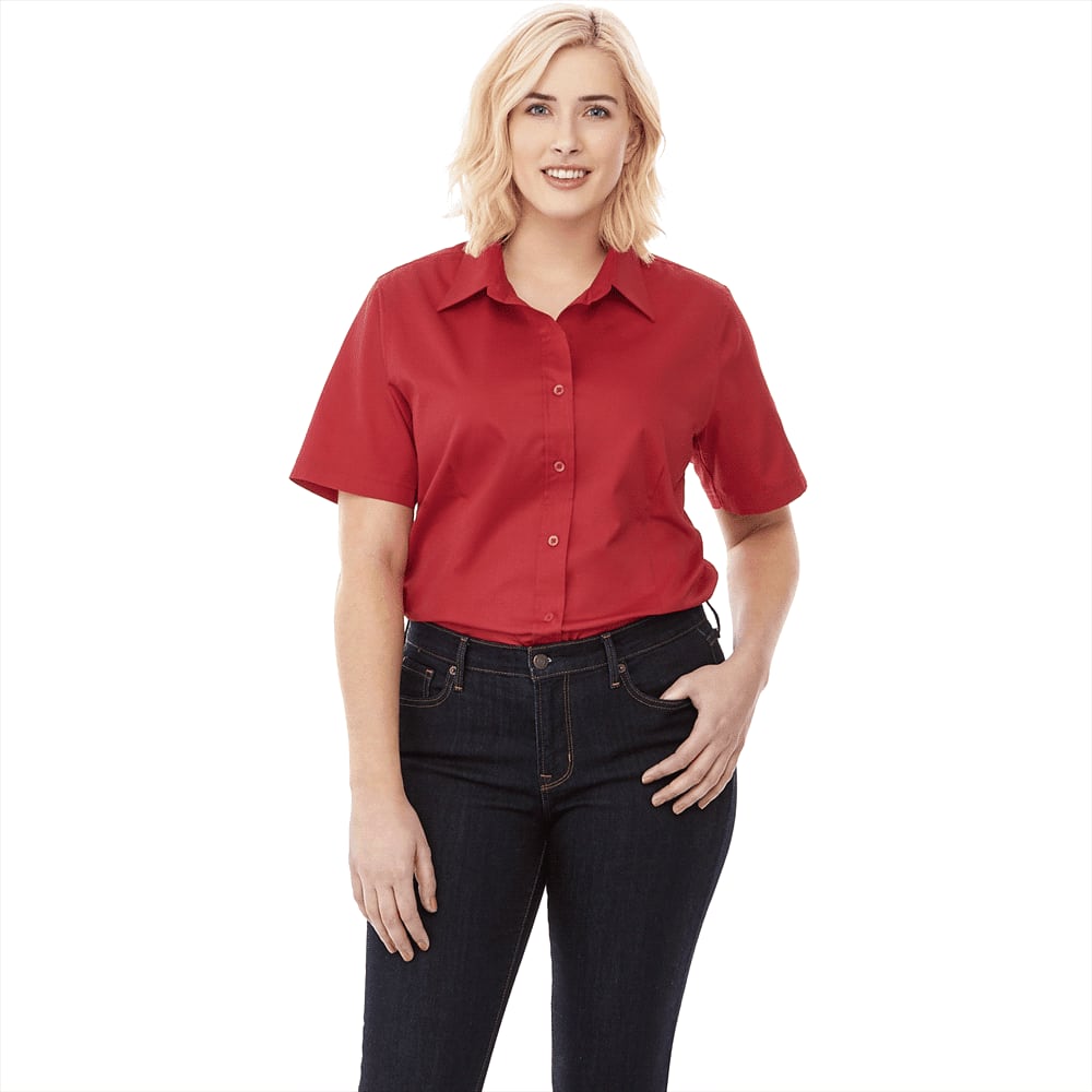 A woman models a red button-up short sleeve shirt paired with dark jeans, featuring a logo on the shirt. Stirling Short Sleeve Shirt - Womens - Image 1
