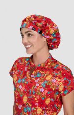 A bouffant cap featuring a vibrant floral print in red, worn by a smiling person. The cap has a logo on it.