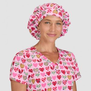 A pink bouffant cap with a heart print, worn by a model in a matching scrubs top with a heart design.