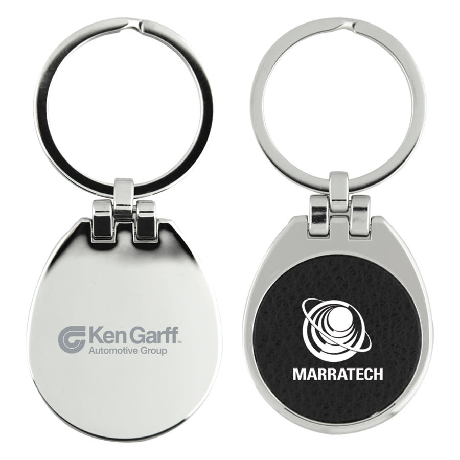 A metallic keychain with a circular ring and a flip top, featuring a textured black surface on one side and logos on both sides. The Westfield Keychain - Image 1