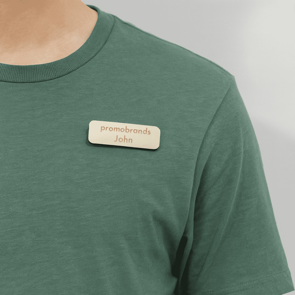 A wooden badge is attached to a green shirt, featuring a branding logo and a name. Complete Magnetic Wooden Badge - Image 1