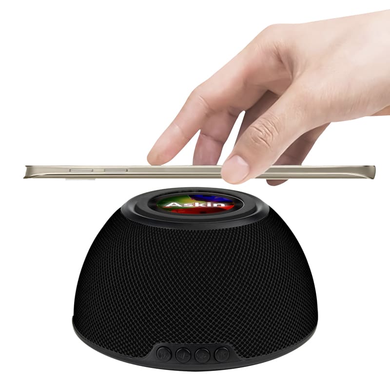 A black wireless charging speaker with a hand positioning a phone above it. It features a logo on the surface. Askin 15W Wireless Charging Speaker - Image 1