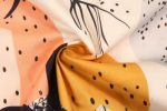 A close-up of fabric featuring a vibrant pattern with peach, orange, black, and cream colours, showcasing a light texture.