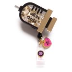 A retractable badge holder featuring black and gold accents with glitter and a charm shaped like a lip gloss bottle.