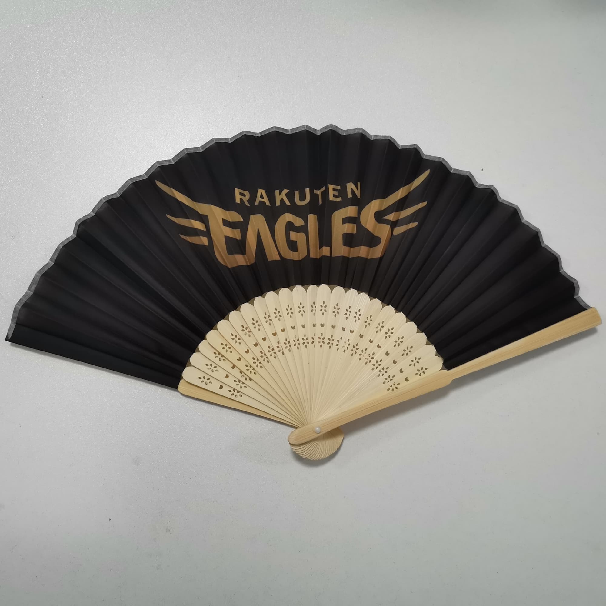 A black bamboo and fabric folding fan with a decorative design and a logo. Bamboo/Fabric Folding Fan - Image 1