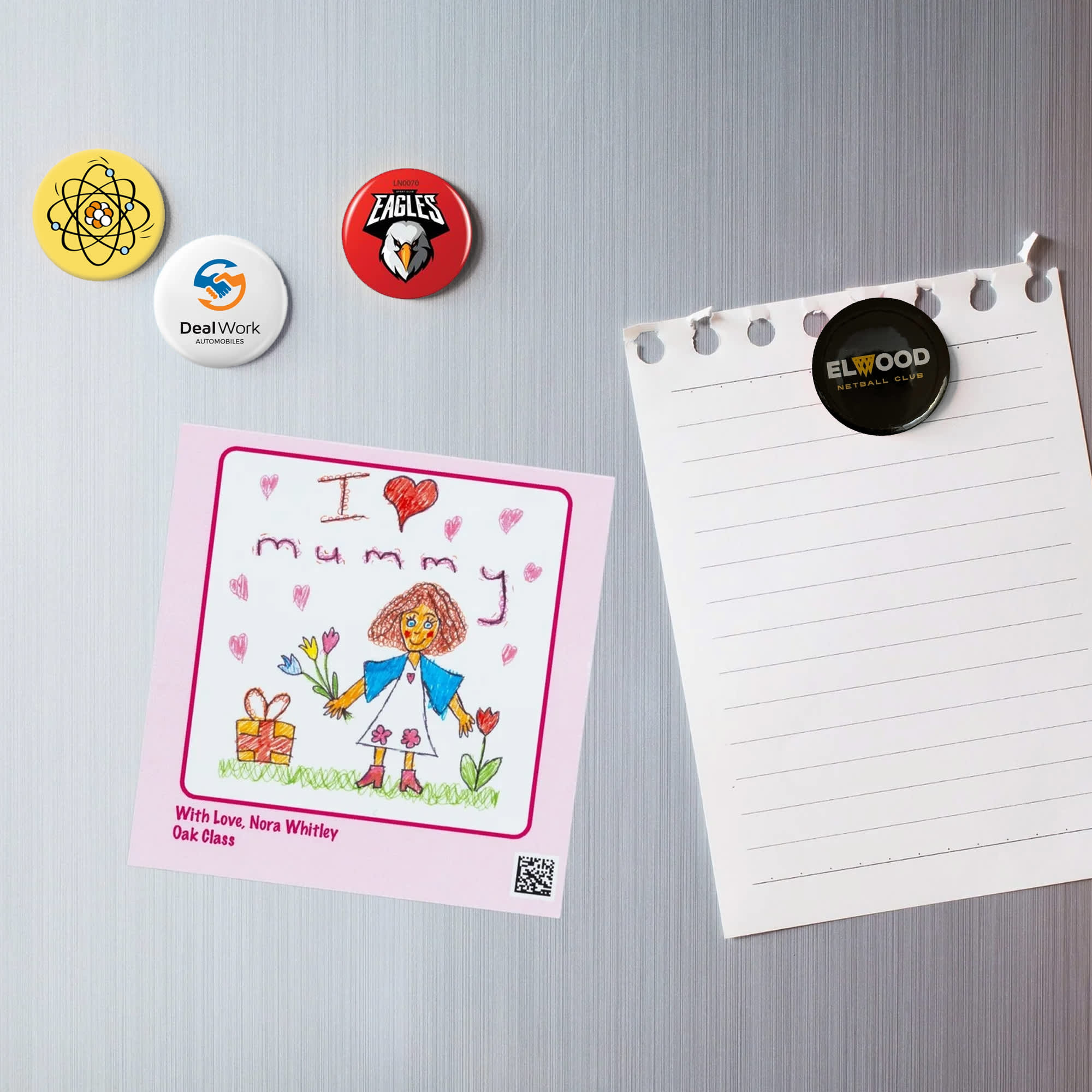 A collection of colourful button badges, including a drawing, displayed on a metallic surface with a notepad. Fridge Magnet Button Badge - Image 1