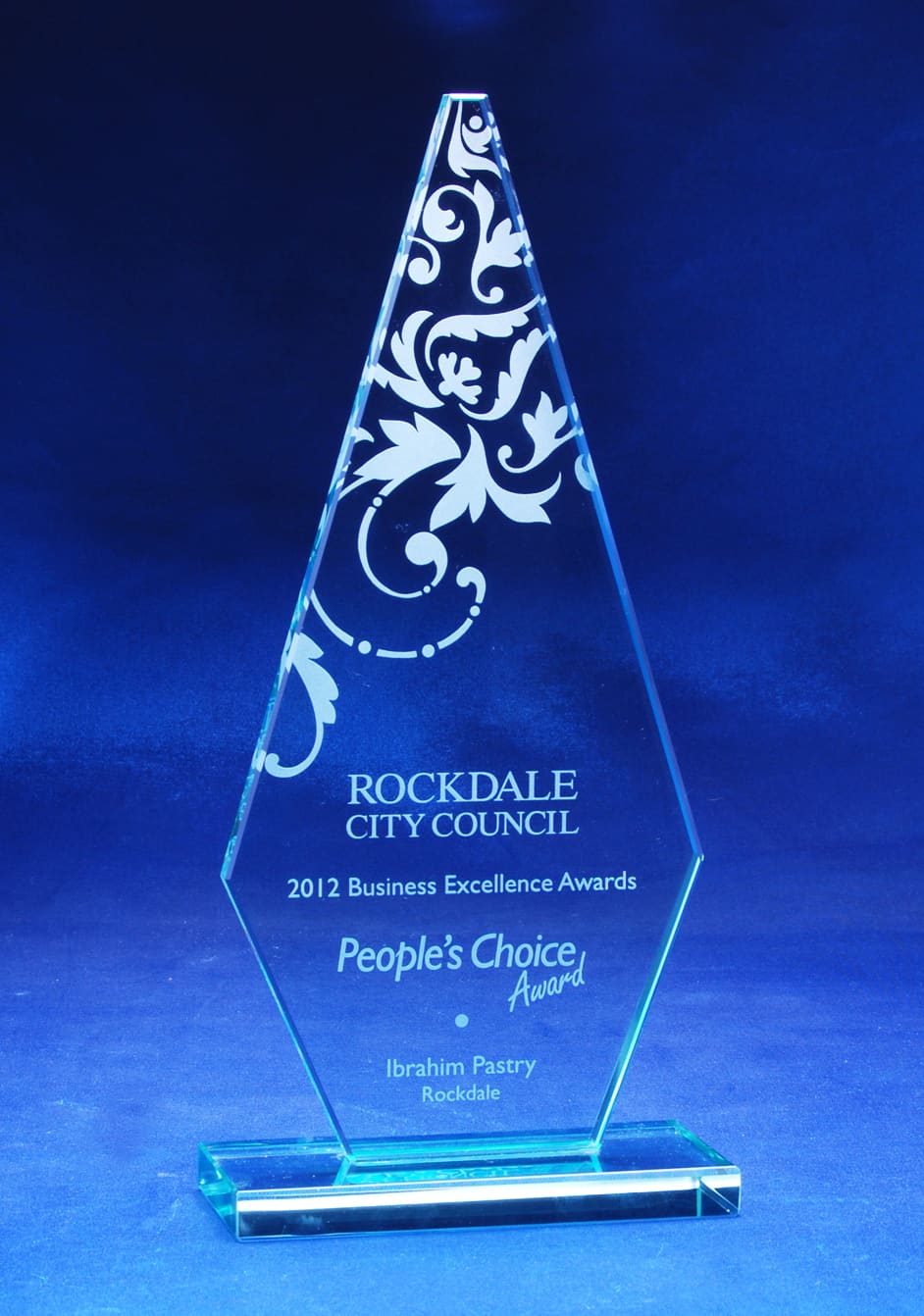 A jade glass arrowhead trophy with decorative etchings, featuring a clear base and set against a blue background. Jade Glass Arrowhead Trophy - Image 1