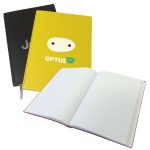 Three A5 recycled notebooks are displayed, featuring a black cover, a yellow cover with a logo, and an open notebook with lined pages.