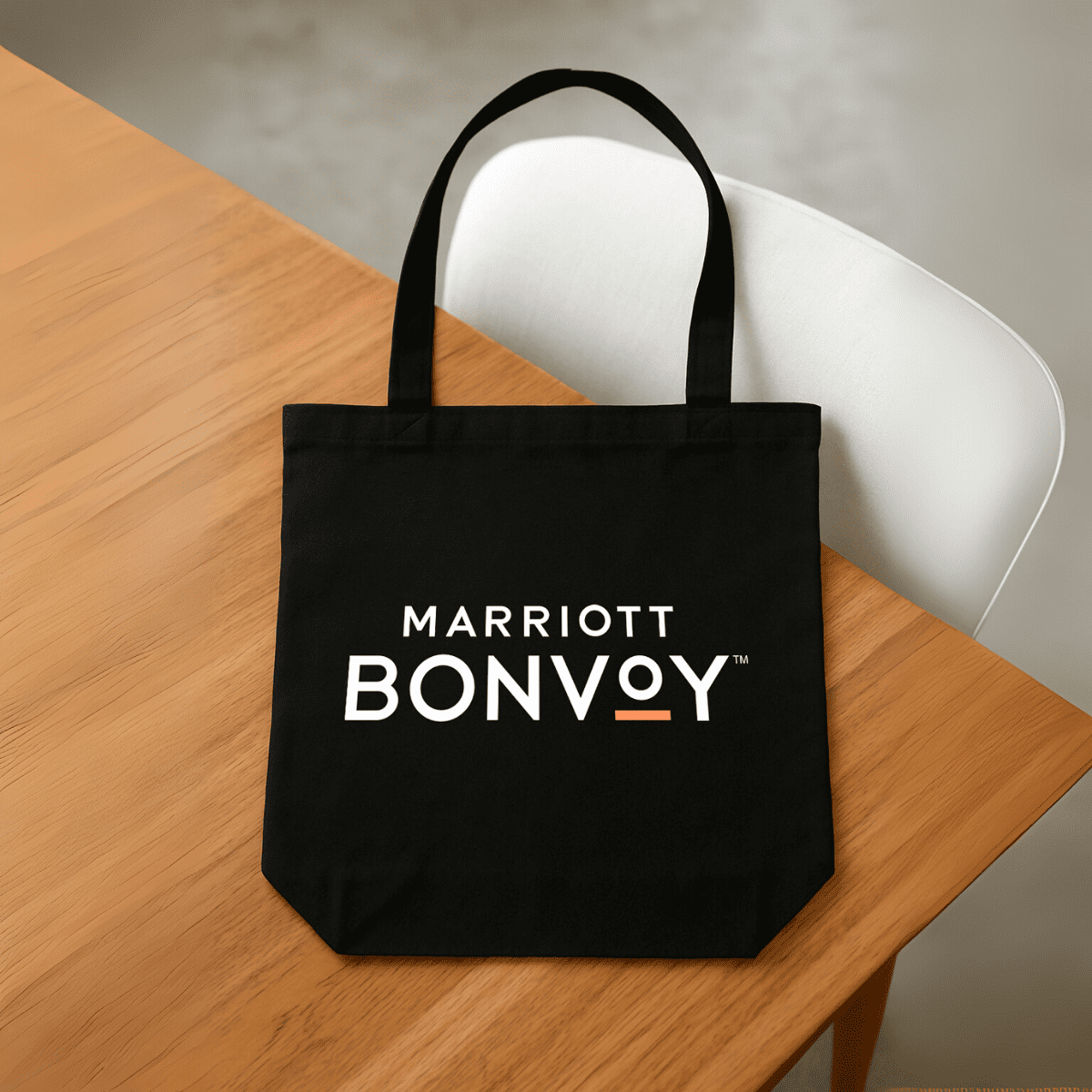 A black tote bag with handles, featuring a logo on the front, placed on a wooden table. Willow Coloured Tote - Image 1