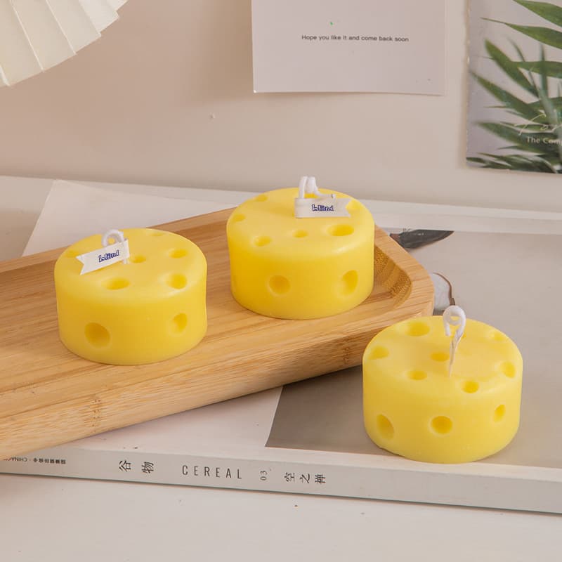 Round cheese-shaped candles in yellow, featuring holes, placed on a wooden serving tray. Round Cheese Shape Candles - Image 1