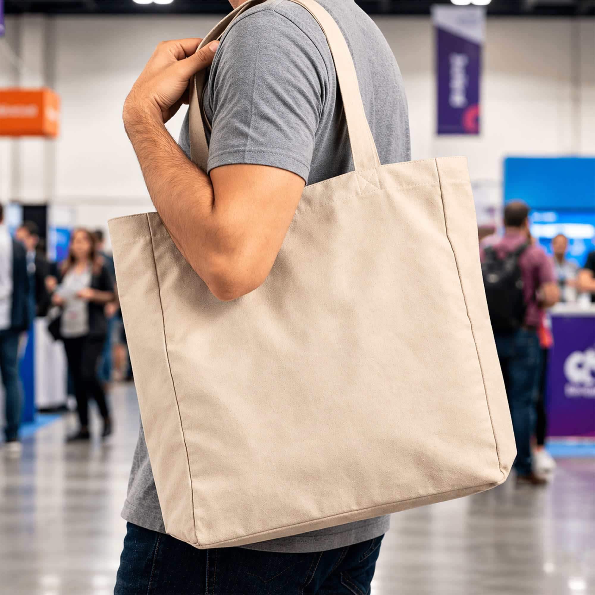 A person holds a beige 450gsm Victorian canvas tote bag with shoulder straps. The bag features a logo. 450gsm Victorian Canvas Tote Bag - Image 1