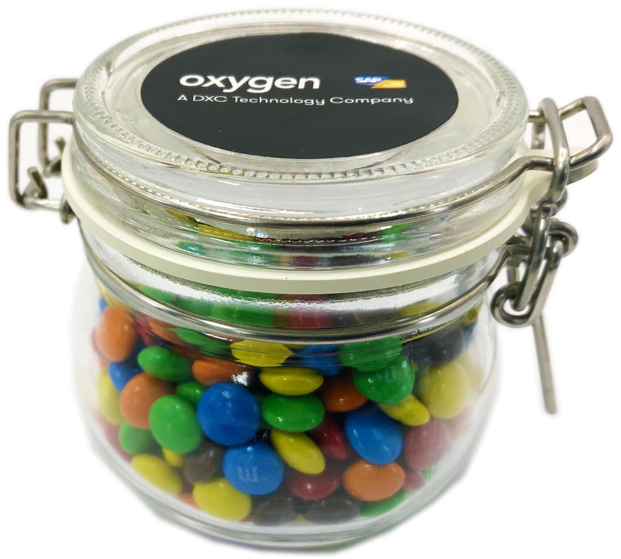 A glass canister filled with colourful mini M&Ms, featuring a metal clasp and a logo on the lid. Small Canister with Mini M&Ms 130g - Image 1