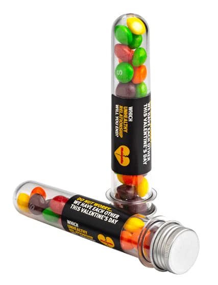 A clear test tube filled with colourful Skittles, featuring a silver cap and a branding label. A clear test tube filled with colourful Skittles, featuring a silver cap and a branding label.