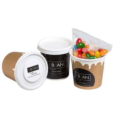 A coffee cup in brown cardboard with a white lid, containing a bag of colourful jelly beans. It features a logo. Coffee Cup With Mini Jelly Beans 50g - Image 1