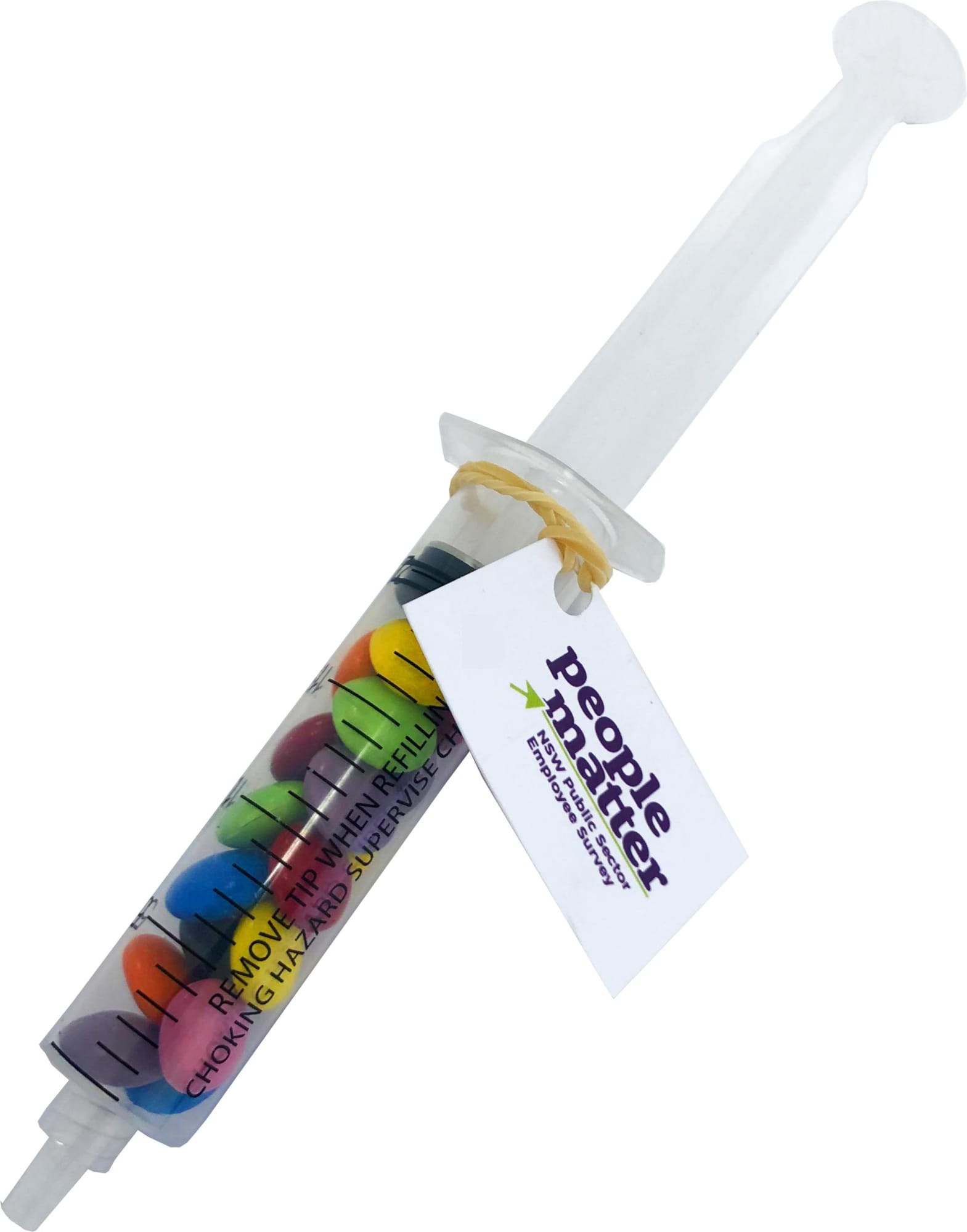 A syringe filled with colourful choc beans in various shades, featuring a tag and a logo. A syringe filled with colourful choc beans in various shades, featuring a tag and a logo.
