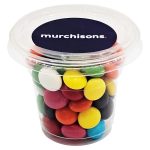 A clear tub filled with colourful choc beans in various shades, including red, yellow, green, and blue.