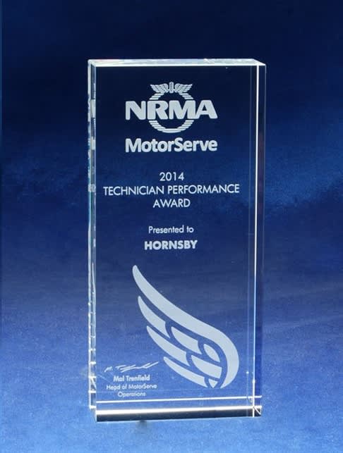 A clear optical crystal monolith award etched with text and a logo, set against a blue background. Optical Crystal Monolith - With Etching - Image 1