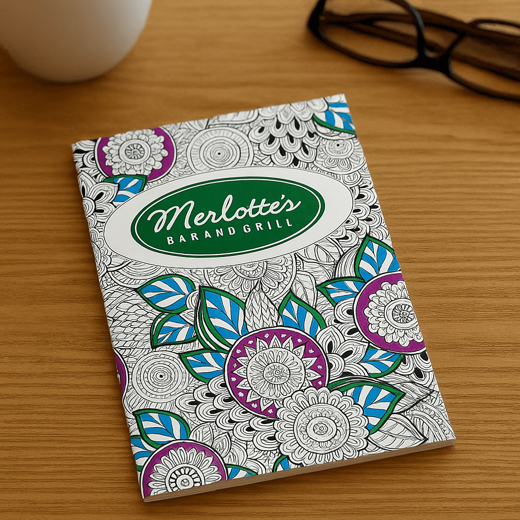 An A4 colouring book with intricate floral designs in purple, blue, and green on a white cover, featuring a logo. A4 Colouring Books - Image 1