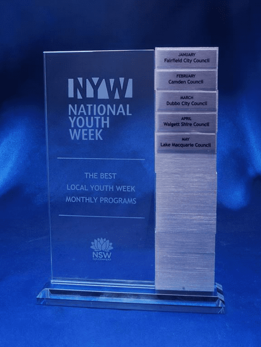 A clear acrylic award with a rectangular base, featuring engraved text and multiple engraved tabs for months and council names. Legacy Tower - Image 1