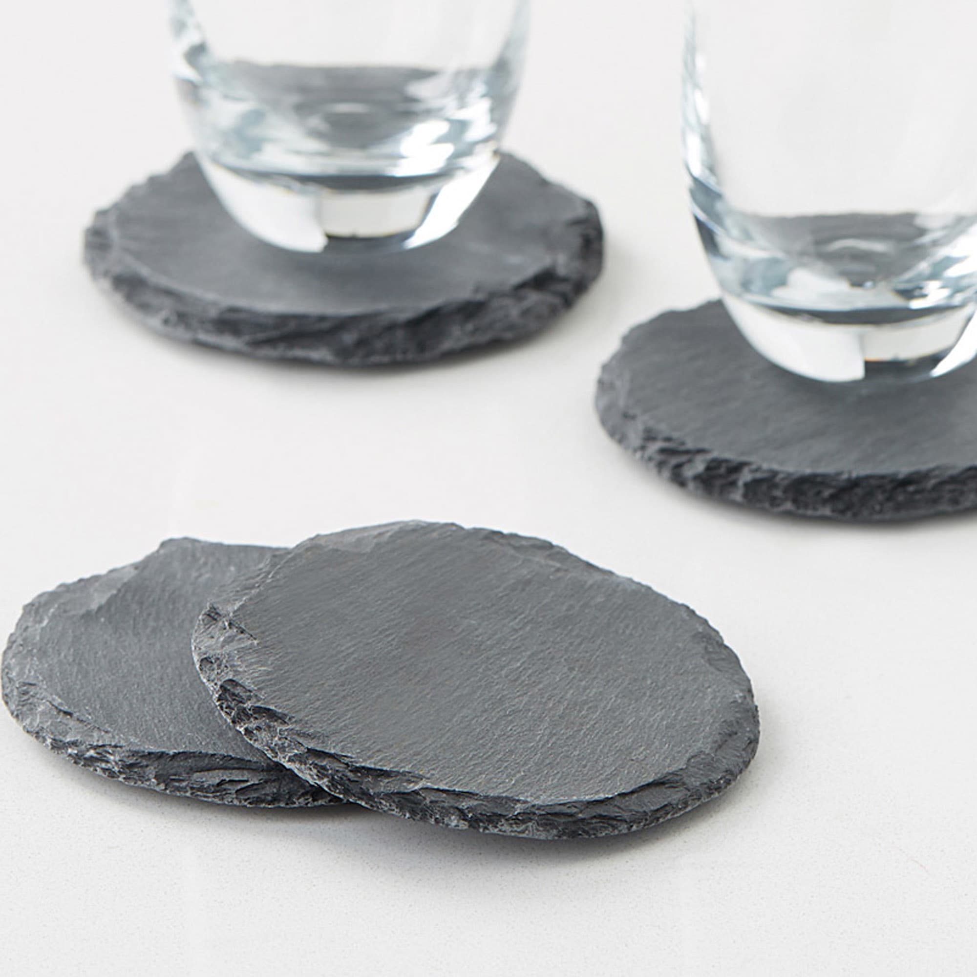 A set of four round slate coasters in grey with textured edges, featuring two glasses resting on them. Slate Coaster Set of 4 - Image 1