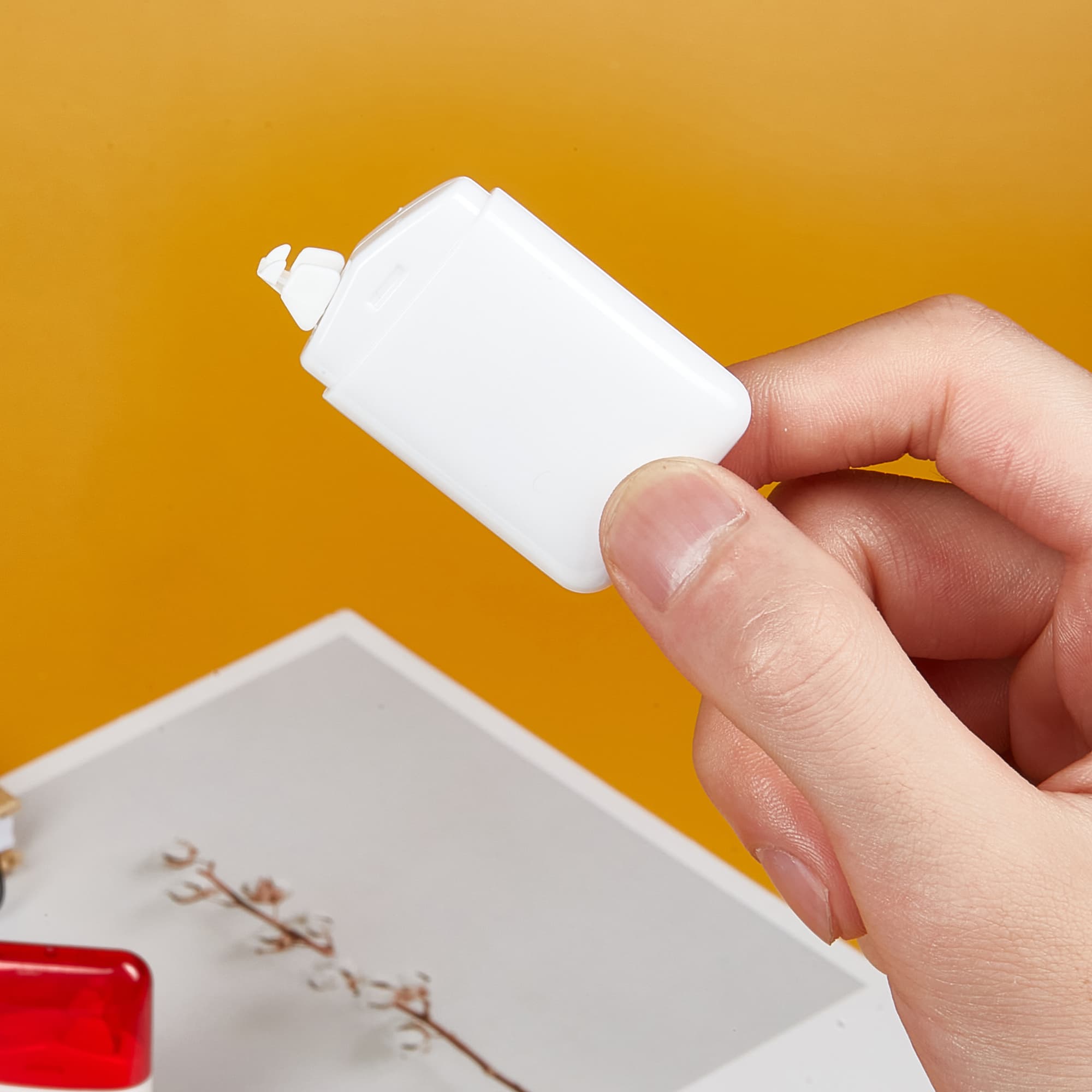 A white correction tape dispenser held in a hand, against a vibrant orange background. Alta 6m Correction Tape - Image 1