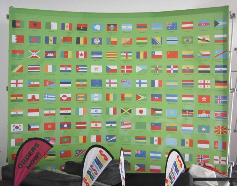 A curved media wall featuring a vibrant green background with various country flags displayed. It has a branding logo. Media Wall 3m x 2.25m - Curved - No Sides - Image 1