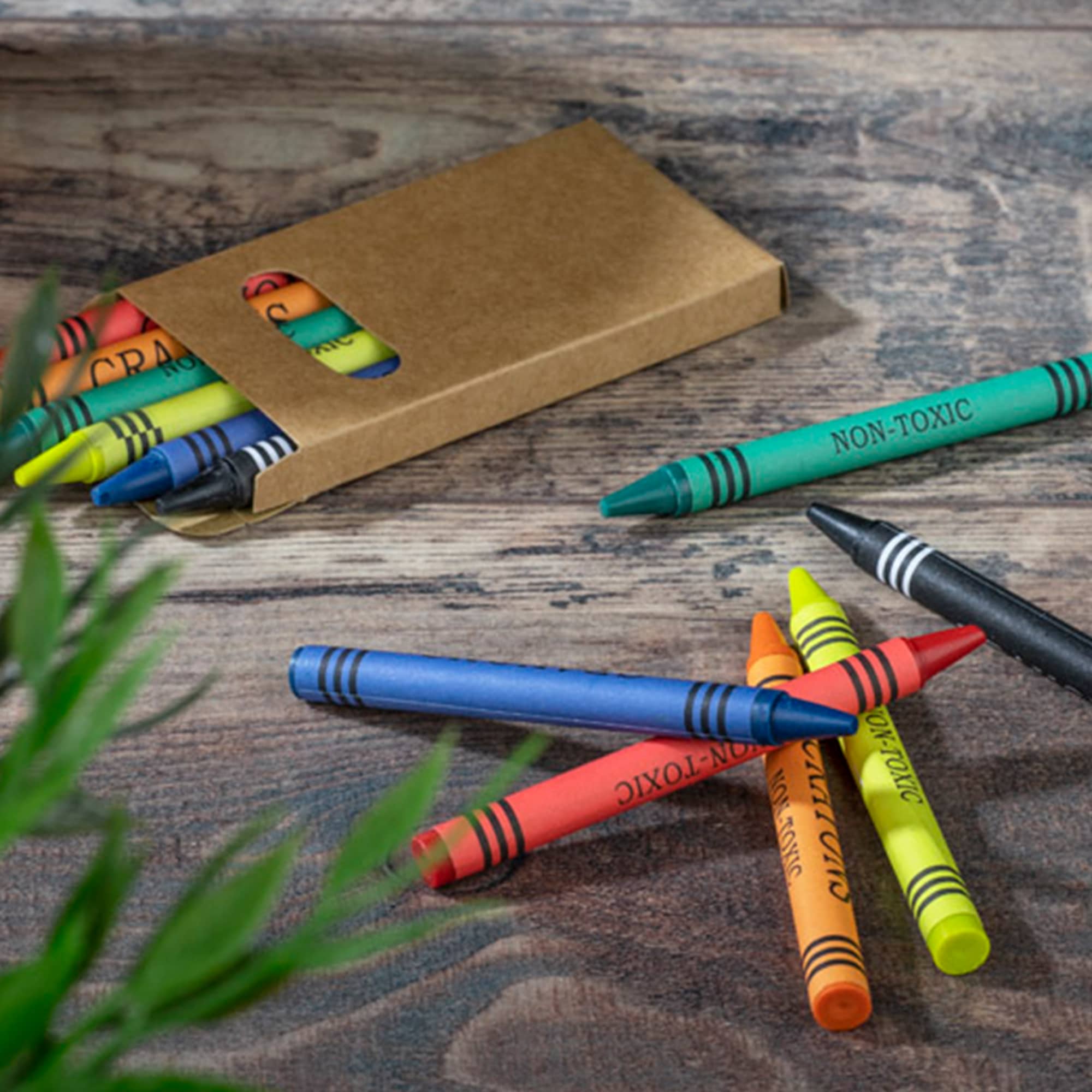 A crayon set featuring six vibrant colours in a cardboard box, with some crayons scattered on a wooden surface. Norva 6CT Crayon Set - Image 1